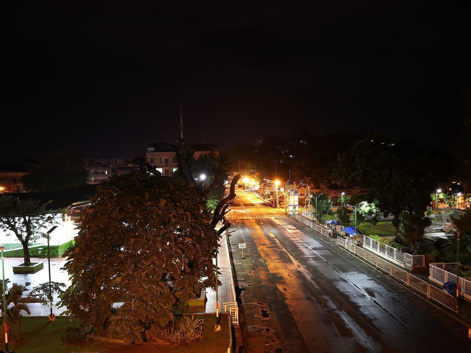 A wet Cotabato City boulevard at night, street lights strung down the avenue.